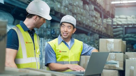 Varastotyöntekijät käyttävät tietokonetta lähetysten keskellä.