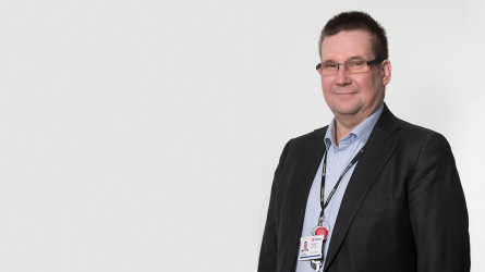 Ville Raevuori seisoo harmaan taustan edessä.