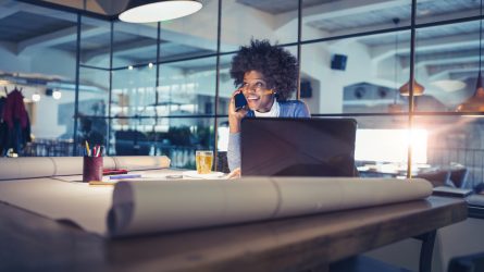 Nainen puhuu pimeässä toimistohuoneessa tietokoneen ääressä puhelimeen.